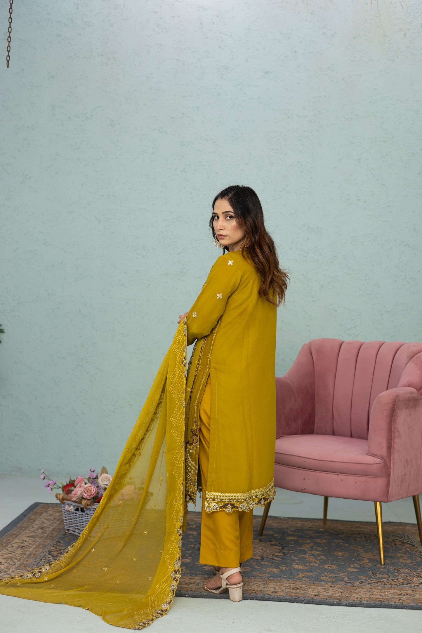 Woman in a light mustard traditional chiffon shalwar kameez outfit standing in a room back picture