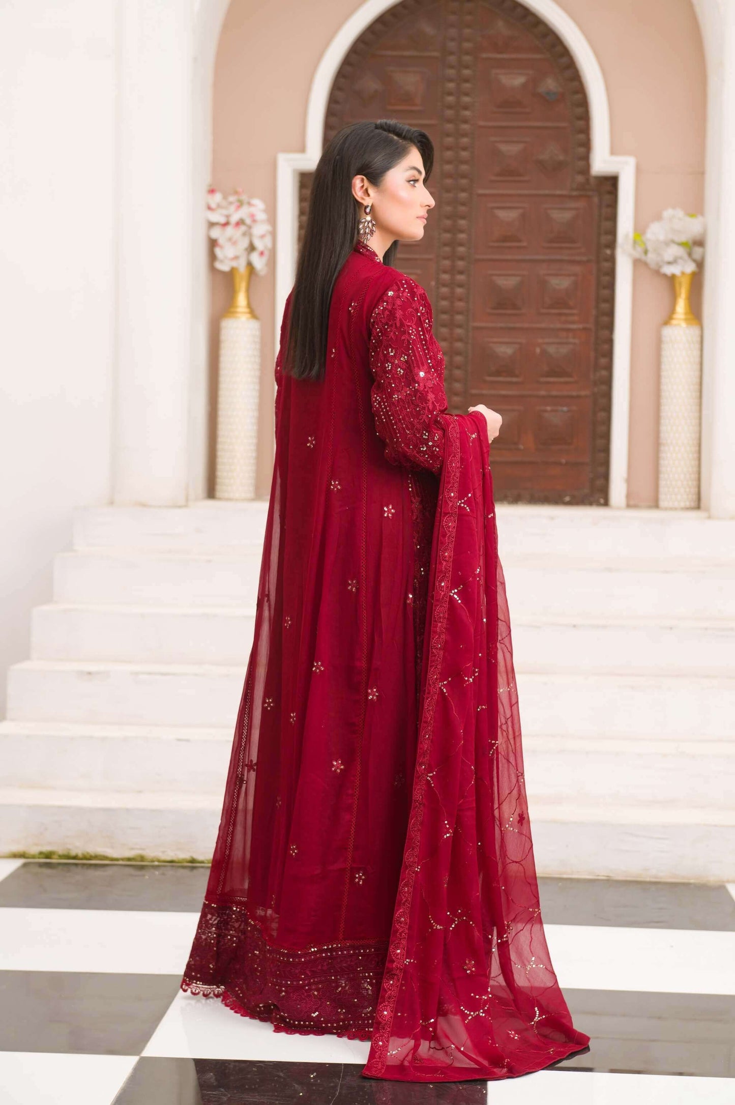 Woman in a red traditional maxi outfit standing in front of a decorative archway back look.