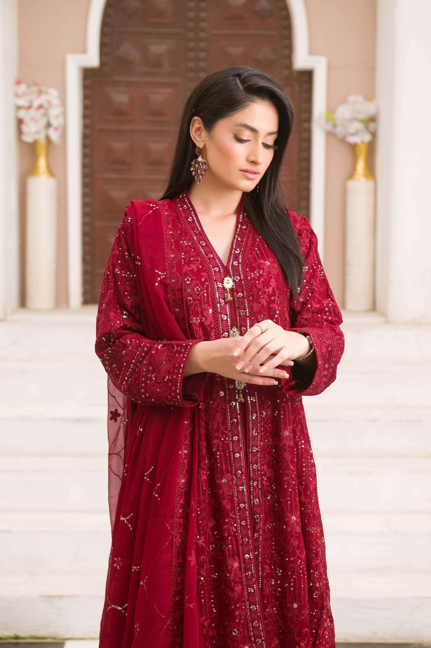 Woman in a red traditional maxi outfit standing in front of a decorative entrance close look.