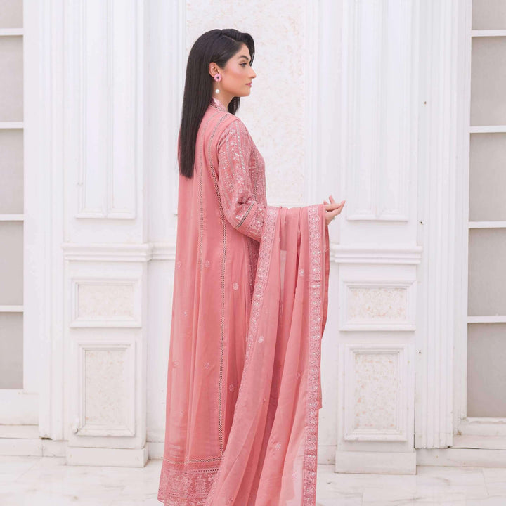 Woman in a pink traditional outfit standing against a white paneled wall back pose