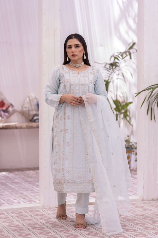 Woman in a light blue embroidered outfit with a white light standing in a decorated room.