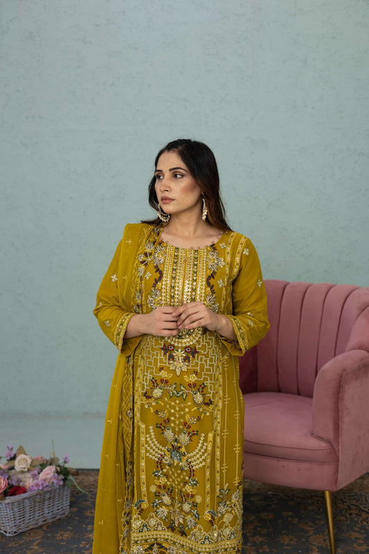 Woman in a light mustard traditional chiffon shalwar kameez outfit standing in a room front picture