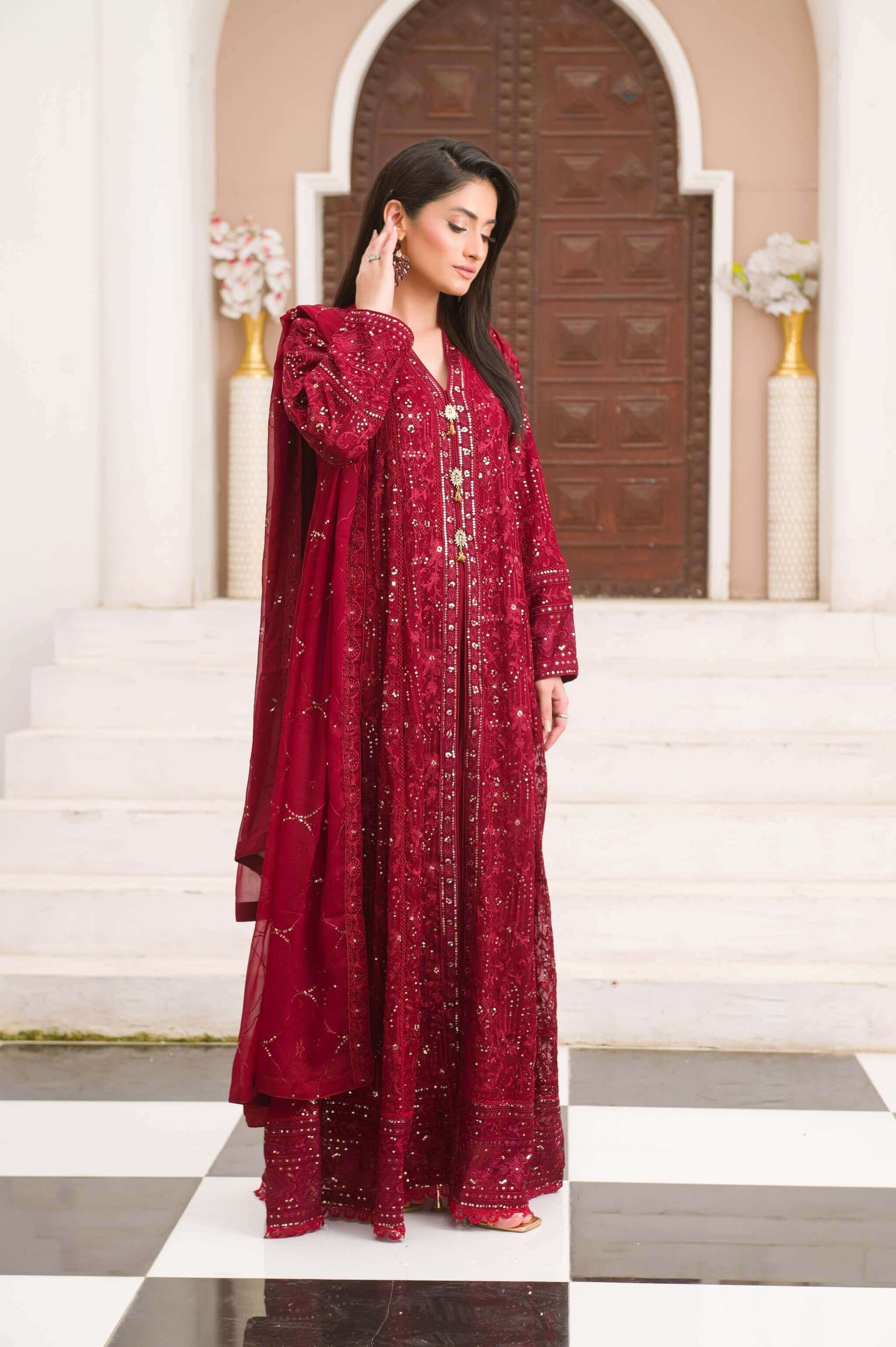 Woman wearing a red embroidered traditional outfit standing in front of a decorative archway side look.